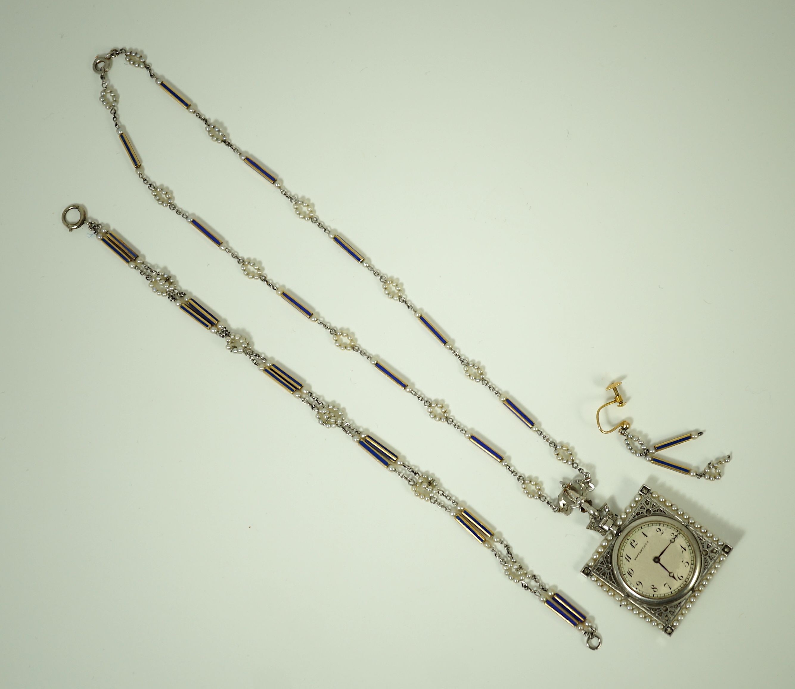 An early 20th century Tiffany & Co platinum, seed pearl and diamond set pendant square open faced dress timepiece, on a platinum, gold, enamel and seed pearl set chain, together with a matching 9ct bracelet and 9ct earri
